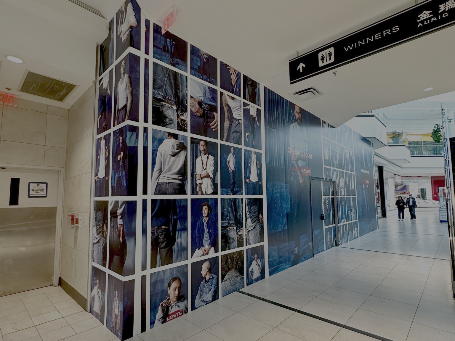 Multi-panel photo collage hoarding graphics wrapping a mall retail unit near Winners