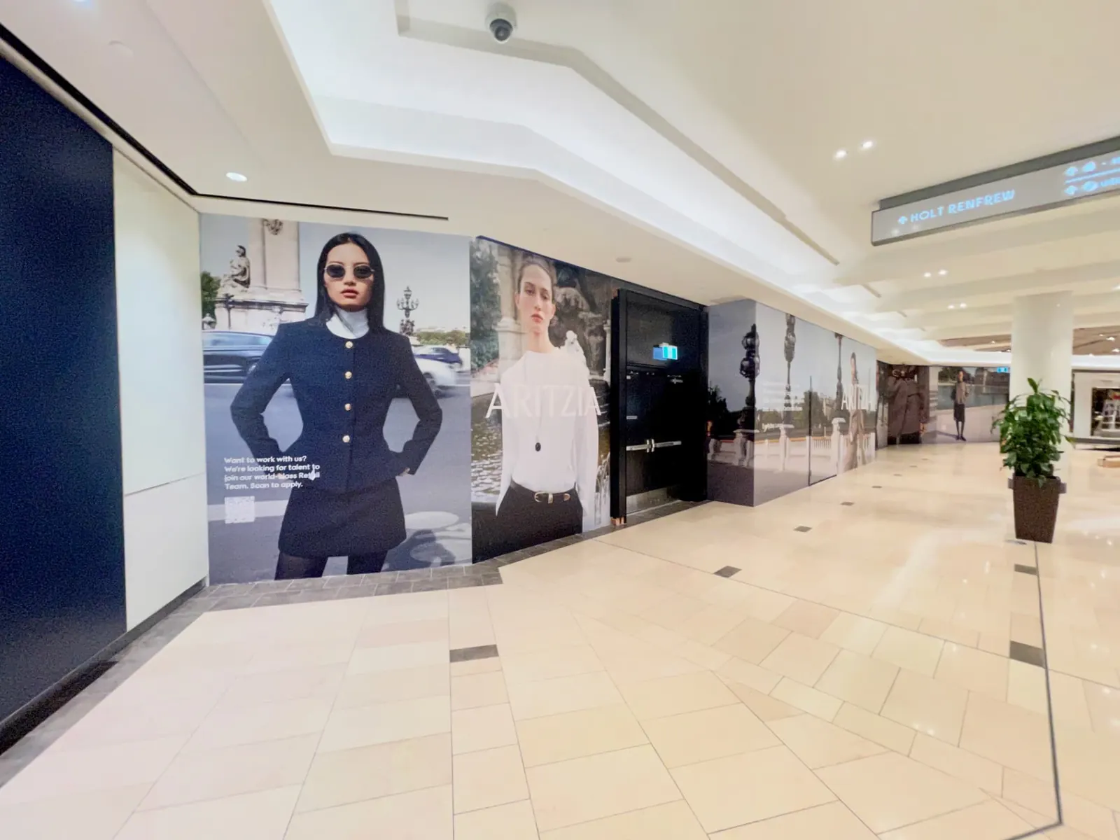 Aritzia hoarding graphics continuing across service doors along a CF Pacific Centre corridor
